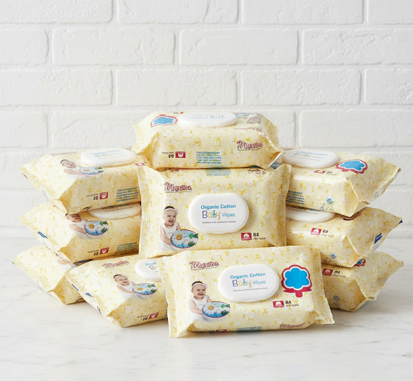 Stack of Maxim Organic Cotton Baby Wipes packs arranged in a pyramid on a marble surface against a white brick wall.