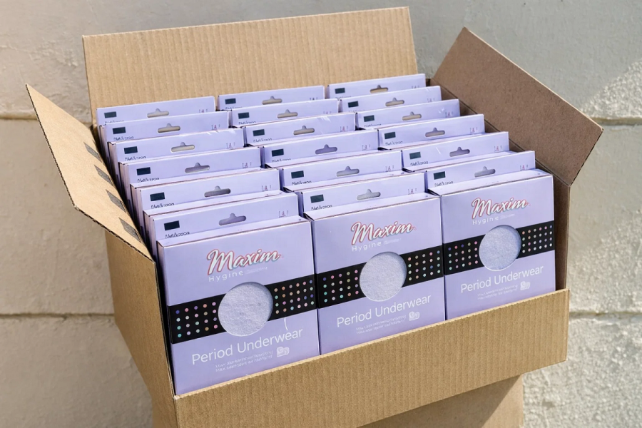 Open cardboard shipping case packed with lavender Maxim ‘Period Underwear’ retail boxes, stacked in rows with hanging tabs visible at the top.