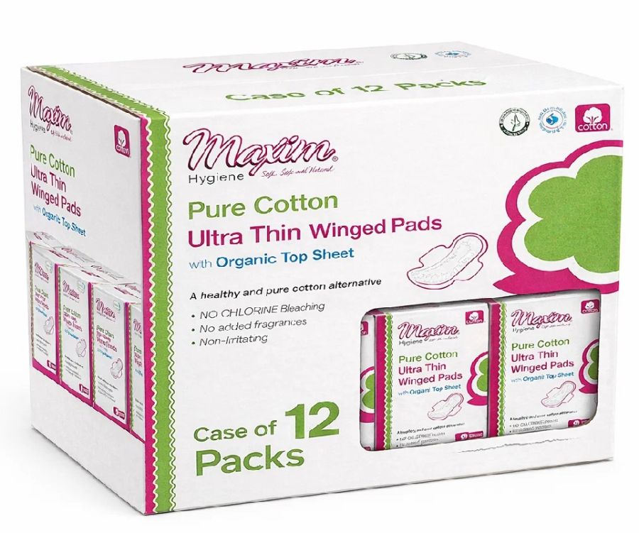 White retail shipping case labeled ‘Case of 12 Packs’ for Maxim Pure Cotton Ultra Thin Winged Pads with Organic Top Sheet. Front shows the Maxim logo, green-and-pink floral graphic, a small pad illustration, and claims: no chlorine bleaching, no added fra